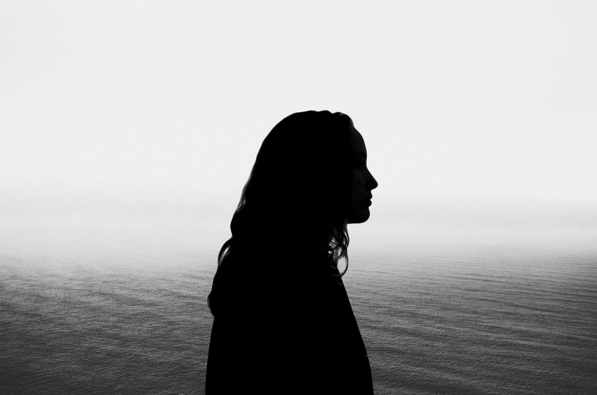 Black and white photo of a person facing right in silhouette in front of water. Annie Suckow, “Reflections VI,” digital photo, 8.5"x11"